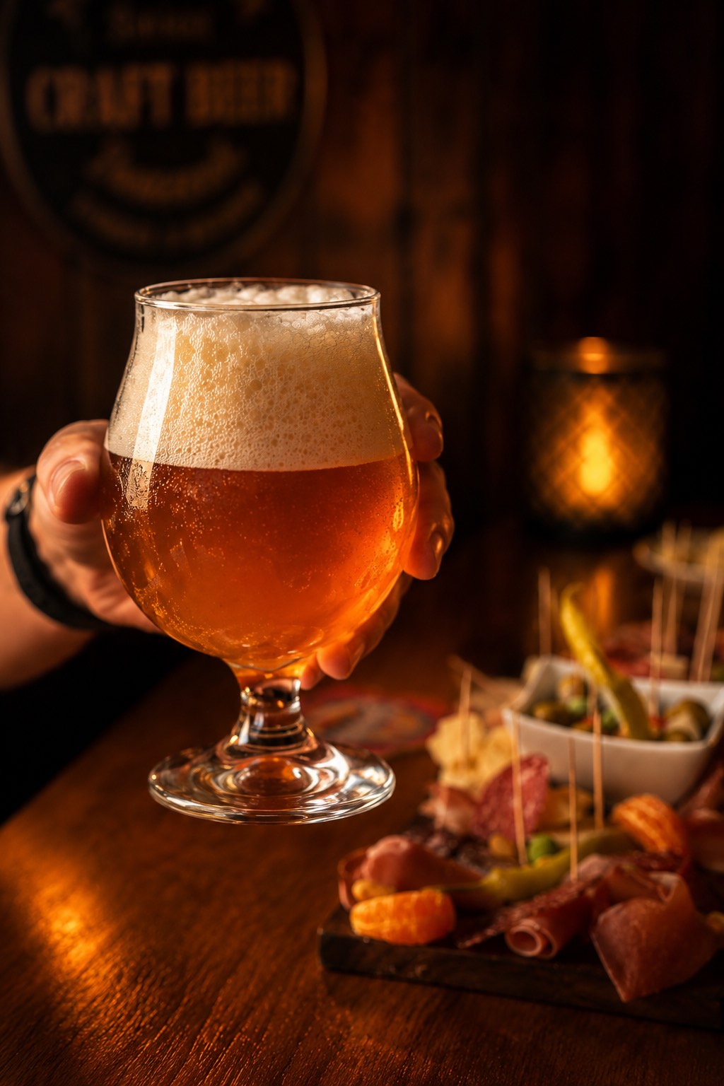 Bière artisanale servie dans son verre, tenue à la main devant une planche de charcuterie