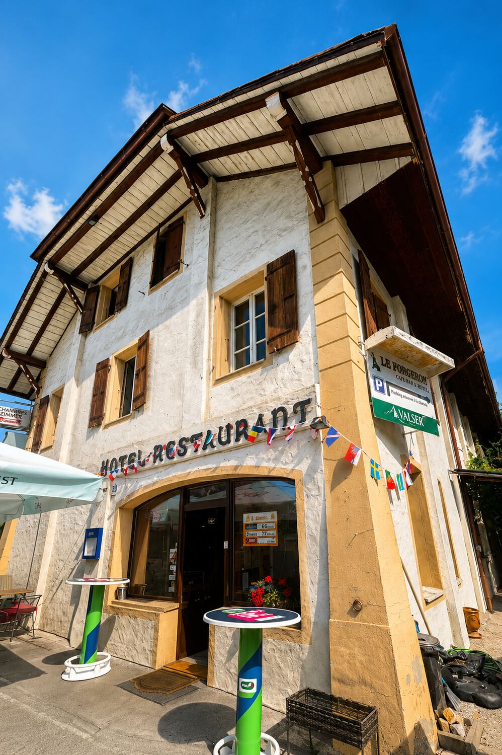 La façade du Forgeron sous le ciel bleu, enseigne et fanions