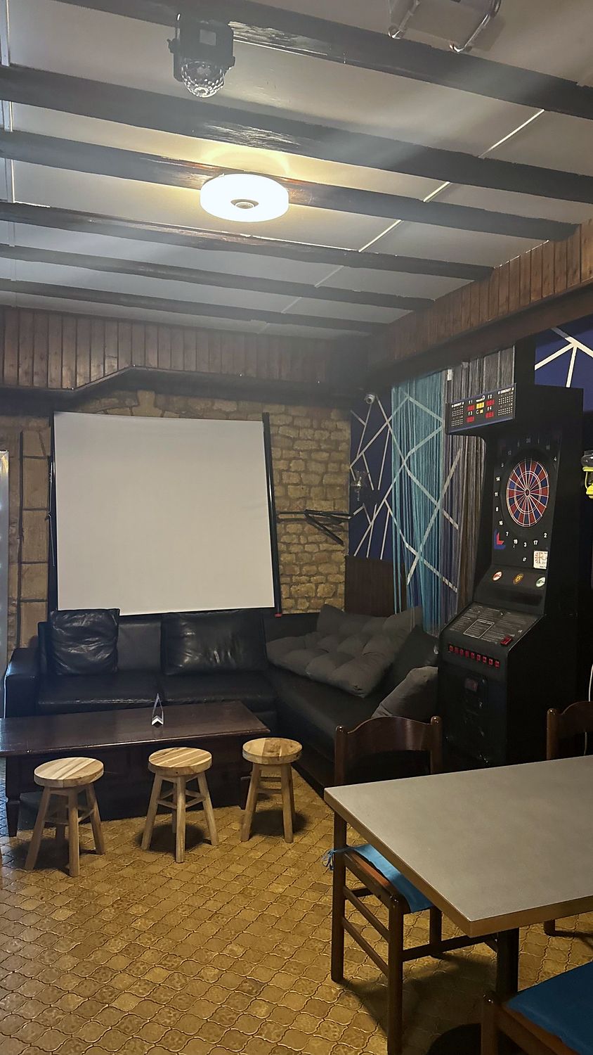 Espace lounge avec écran de projection, dartboard électronique et canapés