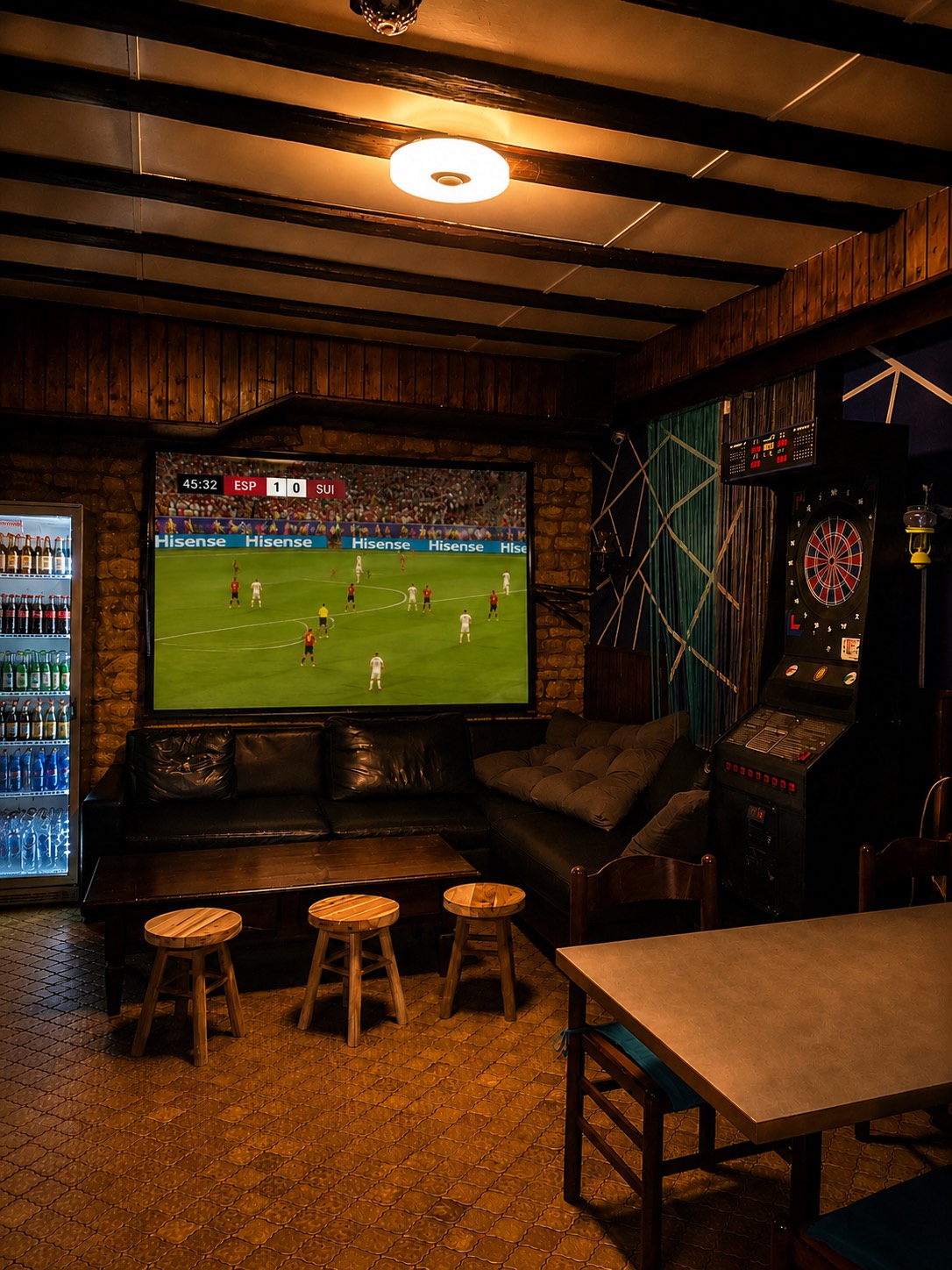 Match de football sur écran géant, fléchettes électroniques et canapés dans la salle du fond